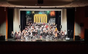 Orchester auf Bühne mit Dirigent, im Hintergrund Bühnenbild mit Brandenburger Tor und Feuerwerk.