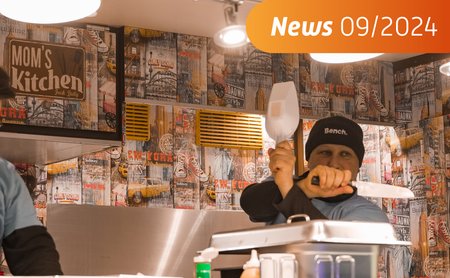 Das Foto zeigt einen Mann in einem Streetfoodwagen, der mit Küchenutensilien handtiert. 