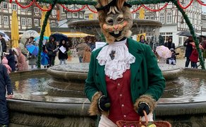Das Bild zeigt eine Frau vor dem Osterbrunnen in Peine, die als Osterhase verkleidet ist. 