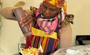 Das Bild zeigt eine Frau aus Afrika, die eine typisch afrikanische Spezialität zubereitet. 