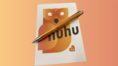 Das Bild zeigt das Peine-Schreibset, einen Blog mit Eulenmotiv und "huhu"-Schriftzug sowie einen Kugelschreiber in orange.