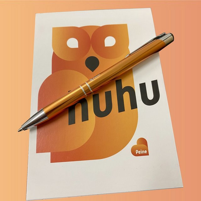 Das Bild zeigt das Peine-Schreibset, einen Blog mit Eulenmotiv und "huhu"-Schriftzug sowie einen Kugelschreiber in orange.