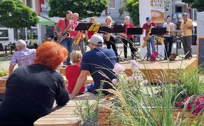 Das Bild zeigt Gäste, die auf der Stadtoase seitzen und einer Band auf der OpenStage in Peine zuhören. 
