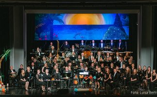 Das Bild zeigt das Stadtorchester Peine auf einer Bühne mit einem blauen Bühnenbild im Hintergrund. 
