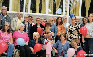 Das Bild zeigt eine Gruppe Menschen, die Luftballons in der Hand halten. 