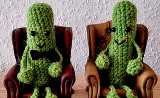 Das Bild zeigt zwei Kakteen, die gehäkelt wurden und auf einem Sessel sitzen. 