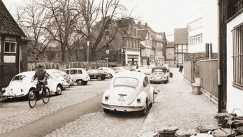 Das Bild zeigt eine historische Ansicht von Peine, ein Straßenzug mit 60er-Jahre Autos.