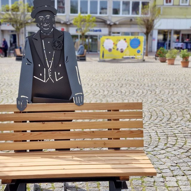 Das Bild zeigt eine  Bank mit Skulptur auf dem Historischen Marktplatz in Peine, was als Kunst im öffentlichen Raum gilt. 