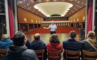 Das Bild zeigt eine Gruppe von Menschen sitzend auf der Bühne des Stadttheaters mit Blick auf den Zuschauersaal.