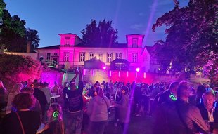 Das Bild zeigt eine tanzende Menge im Burgpark in Peine. Die Szene ist mit Discolicht beleuchtet. 