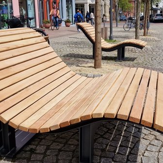 Das Bild zeigt eine Holzliege auf dem Historischen Marktplatz in Peine, was als Kunst im öffentlichen Raum gilt. 